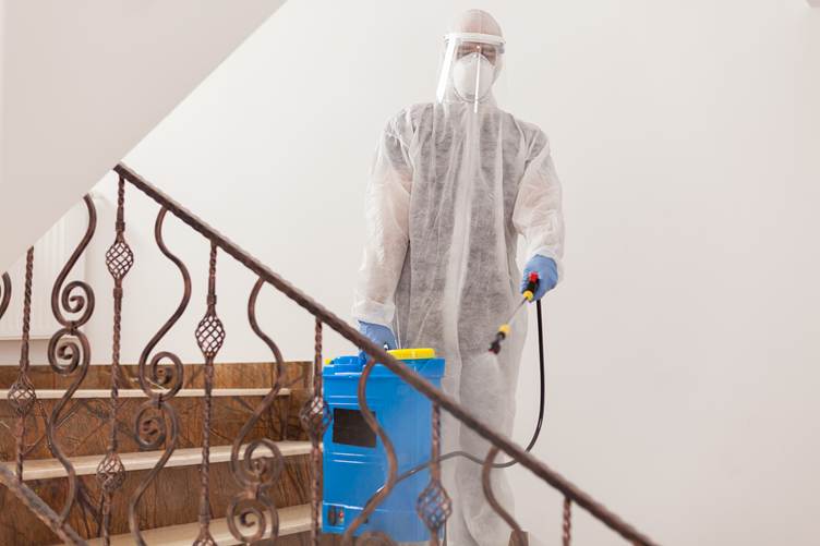 Certified technician in protective equipment spraying disinfectant during residential meth decontamination