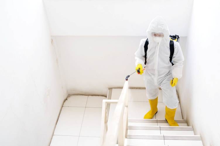 "Certified meth decontamination technician disinfecting an interior staircase in full protective equipment."