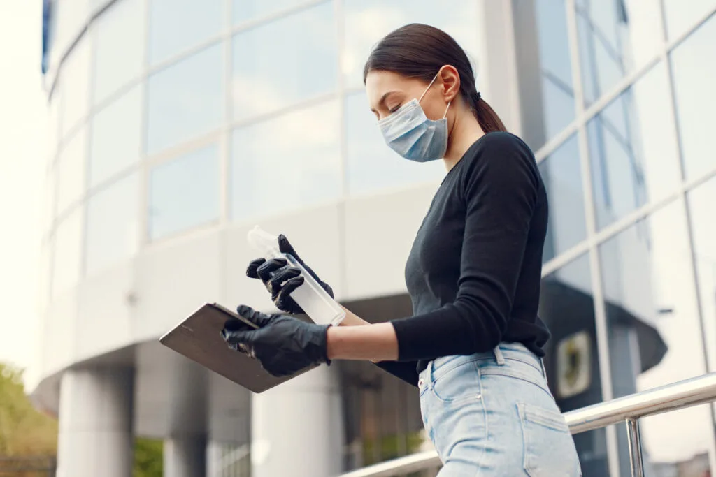 An image of a sanitation worker wearing comprehensive white protective equipment and a respirator mask, standing outside a suburban property during a daytime exterior service visit.